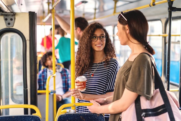 Two girls standing in a bus chatting and drinking coffee.
